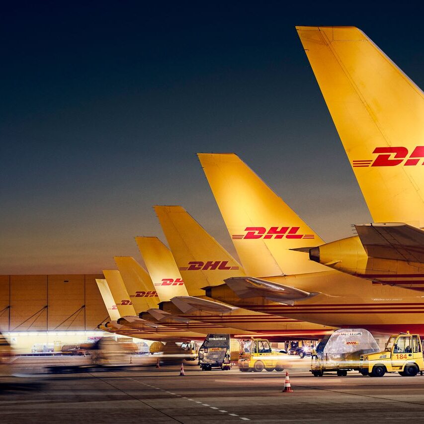 Night shot of the DHL HUB Leipzig. DHL Express turnstile. The rudders of seven DHL aircraft can be seen on the right-hand side of the picture. The hangar is in the background. Transport vehicles are blurred.